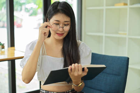 Portrait of female with eyeglasses reading book while waiting for beverage in cafeの写真素材