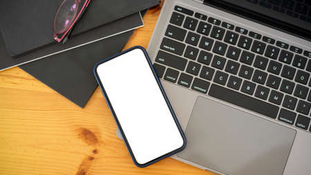 Top view of smartphone with mock-up screen on laptop on wooden workspace with notebooksの写真素材