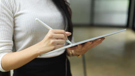 Cropped shot of female hand using digital tablet while standing in office working spaceの写真素材
