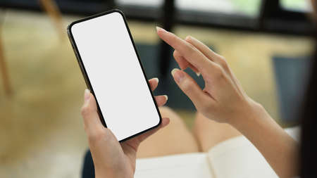 Close up view of female using smartphone with mock-up screen while sitting in workplaceの写真素材