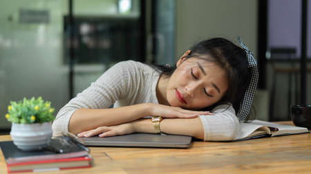 Portrait of young female student take a nap while doing assignment in living roomの写真素材