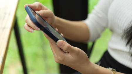 Side view of female using smartphone in her hands while sitting at wooden bar in cafeの写真素材