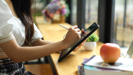 Side view of female hand using digital tablet with stylus pen to do assignment in cafeの写真素材