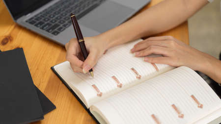 Top view of female handwriting on schedule book while working in workspaceの写真素材