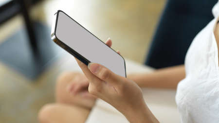 Side view of female hand holding smartphone with mock-up screen while sitting in workplaceの写真素材