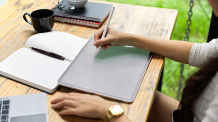 Cropped shot of female hand using digital tablet and stationery on the table in cafeの写真素材