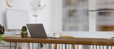 Portable workspace with laptop, cup and cactus pot on wooden table in office room, 3D rendering, 3D illustrationの写真素材