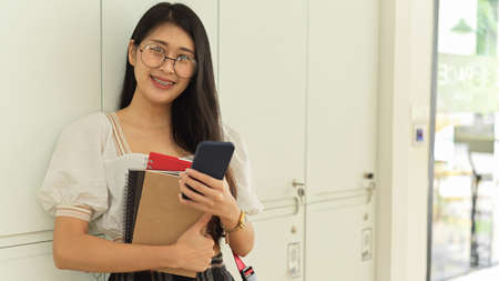 Portrait of female teenager with eyeglasses holding books and smiling to cameraの写真素材