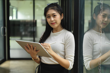 Portrait of female teenager looking into camera while standing and using digital tabletの写真素材
