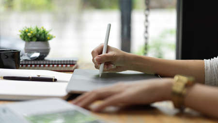 Side view of female hands using digital tablet with stylus pen on the table with stationeryの写真素材