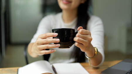 Close up view of female hands holding hot beverage cup and showing to cameraの写真素材