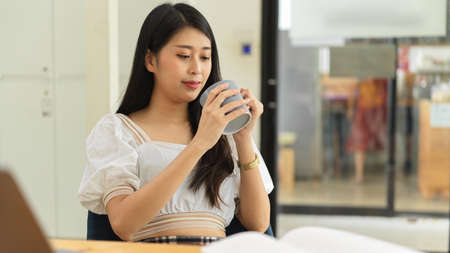 Portrait of female college student drinking coffee while reading book to prepare for examの写真素材