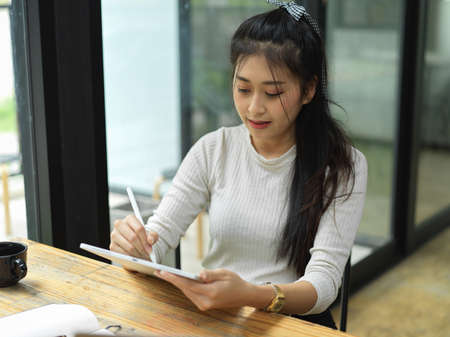 Young female student using digital tablet while sitting in relax corner at homeの写真素材