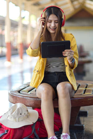 Portrait of female backpacker using digital tablet and headphone while waiting the train in platformの写真素材