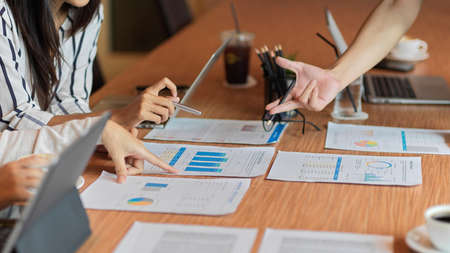 Business concept, closeup of business people discussing on their project with female pointing on papers, reports, office supplies and device on the wooden tableの写真素材