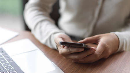 Businesswoman using smartphone with laptop on the wooden deskの写真素材