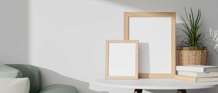 Minimal blank wooden picture frames on white table with minimal wicker plant pot, books and green sofa with white background. 3d rendering, 3d illustrationの写真素材