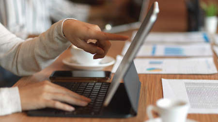 Closeup of businesswoman hands pointing and typing on laptop with the financial papers on the desk...
