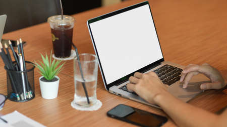 Cropped shot a man working on laptop blank screen at cafe's working space with coffee, mobile phone,...