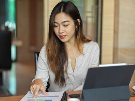 Portrait of businesswoman looking on financial paper with tablet in office roomの写真素材