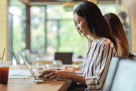 Female employee working and focusing on laptop in the office room with co-workerの写真素材