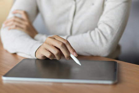 Close up of female using tablet with stylus pen on wooden deskの写真素材
