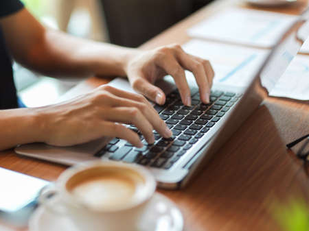 Working woman typing on laptop keyboard with financial report and coffee cup beside on the deskの写真素材