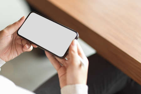 Female hands holding smartphone with white screen for advertising display and blurred backgroundの写真素材