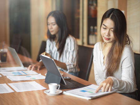 Asian business female workers concentrating their work in the office room with financial report, laptop and coffee cupの写真素材