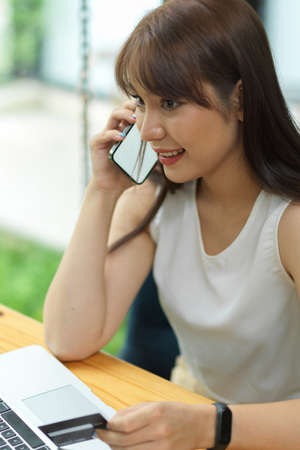 Attractive female making phone call and holding credit card, customer contact seller call centre, mobile phone with blank empty screenの写真素材