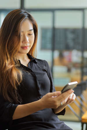Attractive millennial woman sitting and looking on smartphone, Asian teen woman shopping online via her phoneの写真素材
