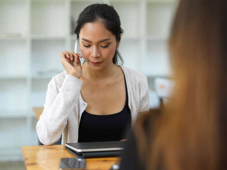 Confident woman looking on tablet while holding stylus pen in front of her friend, Female thinking about her work on tabletの写真素材