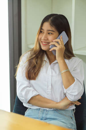 Portrait of attractive casual female making phone call and smiling at officeの写真素材