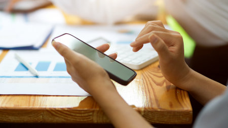 Female texting, touching, using, browsing, contacting on smartphone with blurred office desk in the backgroundの写真素材