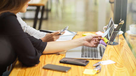 Two company workers talking about their to do list on sticky notes with laptop, device and office supplies at officeの写真素材