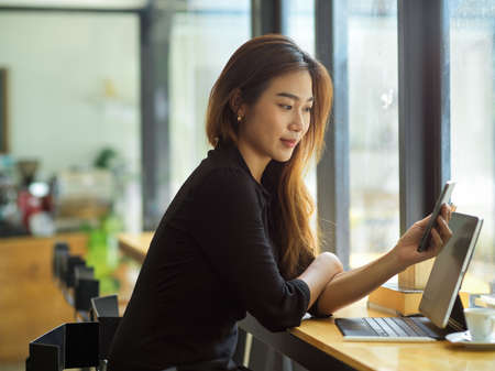 Young attractive woman with casual looks looking on her smartphone with happy face at co-working spaceの写真素材