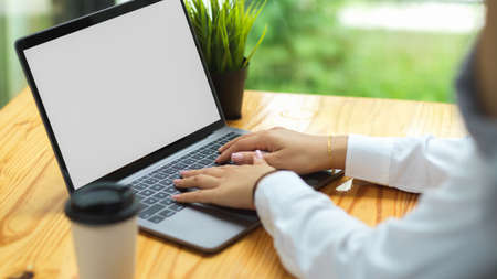 Cropped shot of businesswoman in long sleeve shirts typing on computer laptop with empty white screen at coffee shopの写真素材