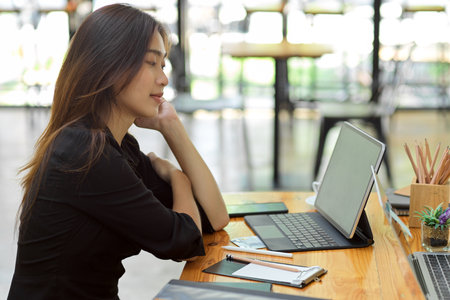 Attractive woman thinking about her job with smart tablet with keypad, stationery at coffee shop co-working areaの写真素材
