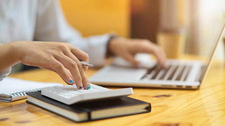 Close up of female accountant fingers using calculator and typing on laptop on wooden tableの写真素材