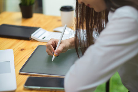 Female drawing on tablet with stylus pen on wooden table at officeの写真素材