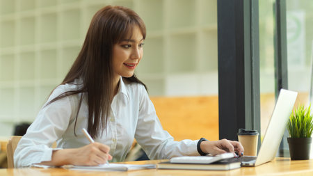 Business student doing lecture on online class via portable laptop at library, E-learning concept, work from home conceptの写真素材