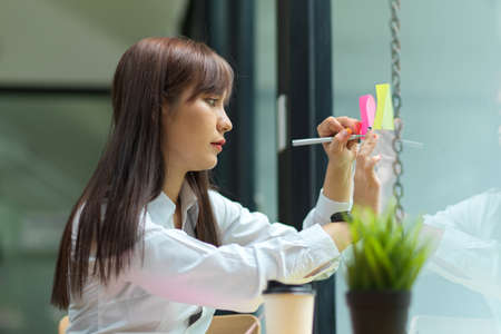 Attractive businesswoman writing her idea on sticky note on the glass window, sharing idea,...