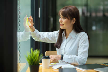 Female sharing the business solution on sticky notes and attaching on the glass window