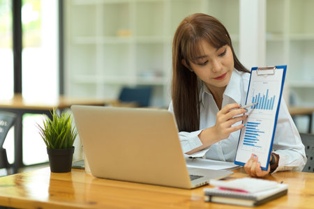 Portrait of attractive business female showing financial bar graph report on online meeting via laptop at officeの写真素材