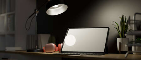 Work space in the dark room, light from table lamp, blank screen smart tablet with headphone and decor, work in evening, 3d rendering, 3d illustrationの写真素材