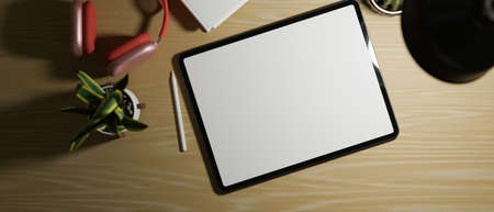 Tablet blank screen on work space with red headphone, house plant and light from table lamp, dark...