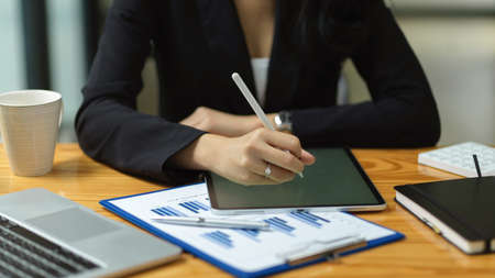 Close up of businesswoman hand are working on smart digital tablet at office, working on financial statement online, stylus pen, reports, laptop on wooden tableの写真素材