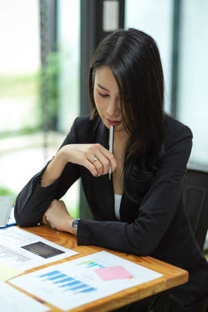 Business female focusing and thinking about her budget working plan with financial reports at office, woman in black suitの写真素材