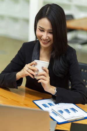 Portrait of young businesswoman manager holding coffee while online meeting via laptop at officeの写真素材