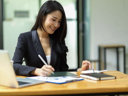 Young asian CEO female calculating project budget via smart digital tablet and calculator at modern officeの写真素材